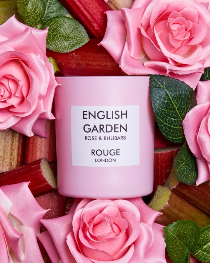 Rouge London English Garden candles displayed with fresh pink roses and rhubarb stems.
